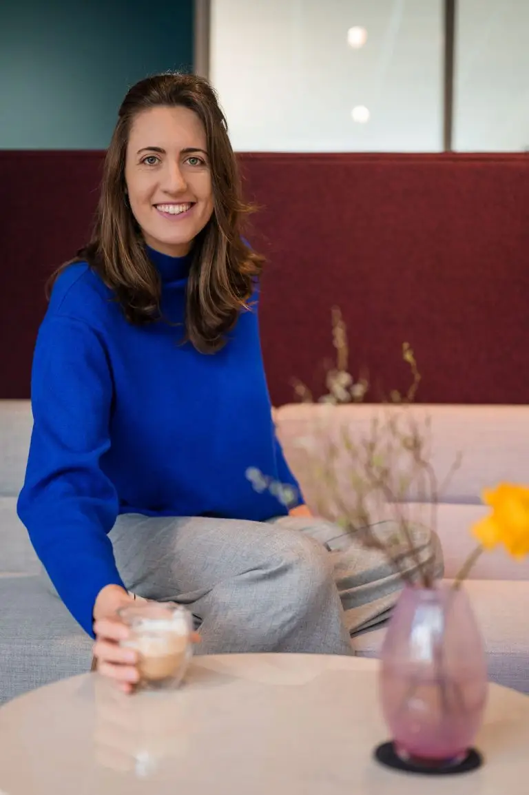 Rebecca greift nach ihrem Kaffee und lächelt in die Kamera