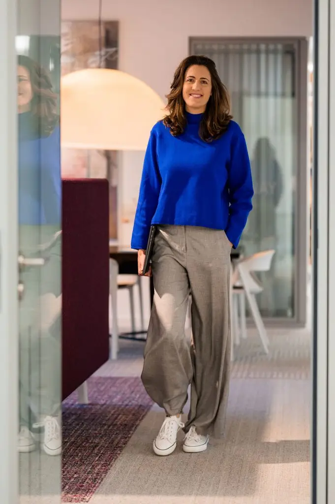 Rebecca läuft mit einem Laptop unter dem Arm auf die Kamera zu.